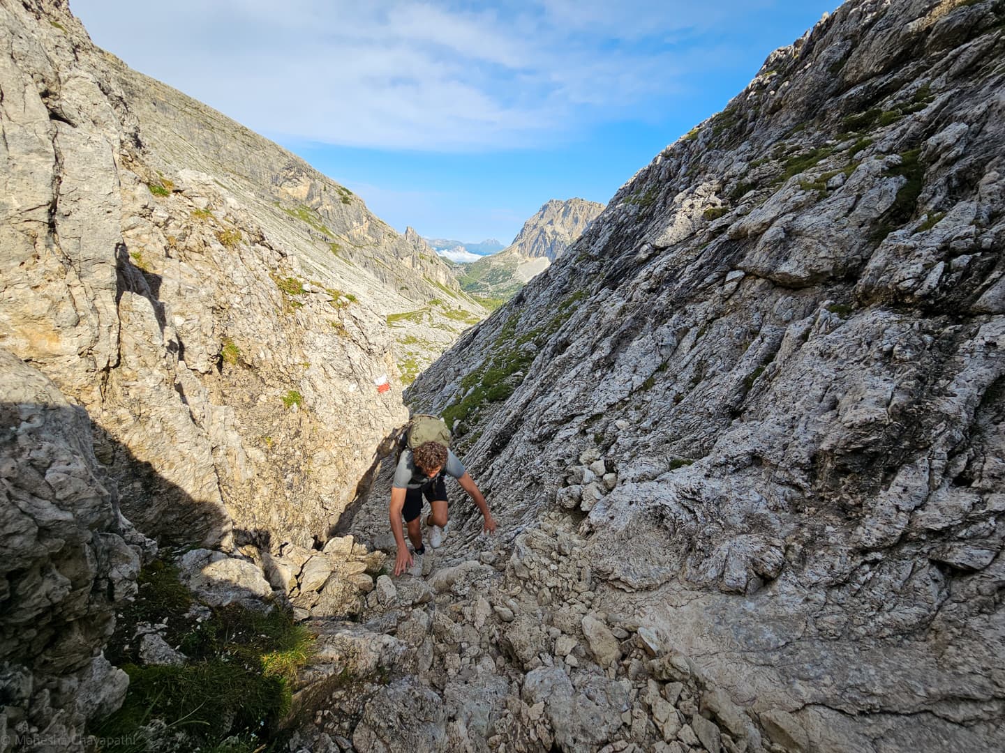 A hiker climbing a steep gully on hands and feet